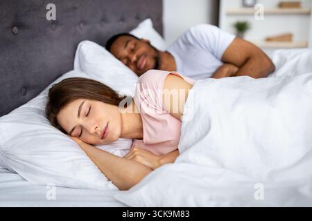 Die junge kaukasische Frau und ihr schwarzer Mann schlafen zu Hause im Bett. Liebevolle Beziehung Stockfoto