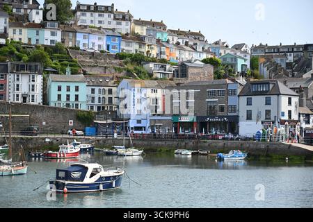 Hafen mit Fischerbooten und Yachten vor farbenfrohen Hügelhäusern und Restaurants am Wasser in einer malerischen britischen Küstenstadt. Stockfoto