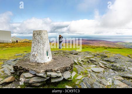 Laxey, Isle of man 08,05,2023 Mann macht ein Foto von einem Berggipfel mit einem weißen Marker drauf. Der Marker ist auf einem Felsen und der Mann steht auf Stockfoto
