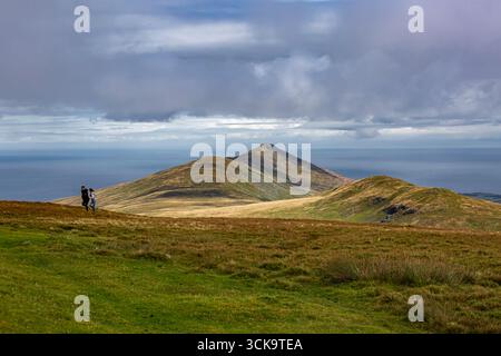 Laxey, Isle of man 08,05,2023 Paar läuft auf einem grasbewachsenen Hügel mit Blick auf das Meer. Der Himmel ist bewölkt und die Aussicht ist atemberaubend Isle of man - Stockfoto