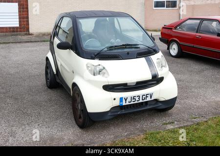 Kompaktes weißes Smart Four two Auto, das in einer Einfahrt mit rotem Fließheck in der Nähe eines Wohngebietes geparkt ist Stockfoto