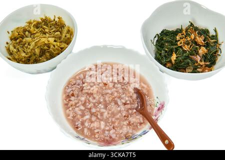 Ein traditionelles thailändisches Frühstück mit gekochter Reissuppe mit Beilagen aus eingelegtem Senfgrün und gebratenem Gemüse, isoliert auf weiß. Stockfoto
