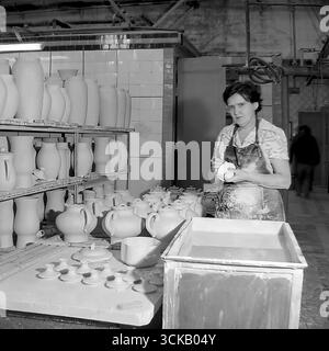 Eine Arbeiterin in der Verglasungswerkstatt des Sloviansk Ceramic Mähdreschers (Ukrainische SSR) an ihrem Arbeitsplatz in den 1980er Jahren Das Archivfoto zeigt eine Arbeiterin einer gebeizten Schürze während der Verarbeitung von keramischen Produkten, im Hintergrund mit ungebrannten Töpferregalen. Dieses realistische Produktionsporträt vermittelt die harten Arbeitsbedingungen und zeigt gleichzeitig die würde und Professionalität einer sowjetischen arbeitenden Frau Stockfoto