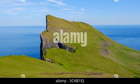 Eine atemberaubende Felsformation erhebt sich dramatisch aus der lebhaften grünen Landschaft und bietet atemberaubende Ausblicke auf den Ozean darunter. Mylingur Färöer Inseln Stockfoto