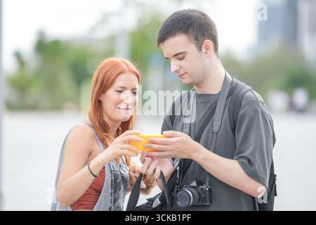 Ein Mann und eine Frau schauen sich ein Handy an. Der Mann hält eine Kamera und die Frau hält ein Handy Stockfoto