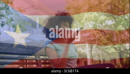 Aufnahme einer afroamerikanischen Frau, die auf der Veranda Telefon zu Mund hält, mit Puerto-ricanischer Flagge Stockfoto
