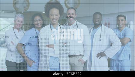 Posierendes medizinisches Team mit blauen Peelings und Stethoskopen in der Lobby der Klinik, mit überlagerten Liniendiagrammen Stockfoto