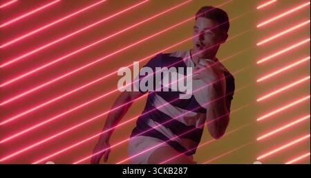 Ein tretender Mann mit marineblauem weiß gestreiftem Polo und weißen Shorts im Studio, mit rosa Neonbalken Stockfoto