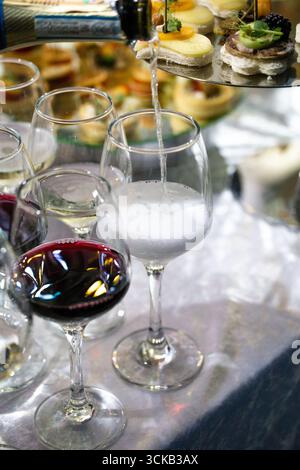 Champagner wird in eine Flöte gegossen, umgeben von Weingläsern und Gourmet-Häppchen auf einem silbernen Tablett, elegante Festatmosphäre für Hochzeiten oder lu Stockfoto