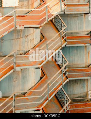 Verrostete Metalltreppen mit industrieller Textur, Poster-Dekoration. Repetitive Zickzacktreppe mit abblätternder Farbe und korrodierten Oberflächen auf einem verwitterten Metall Stockfoto
