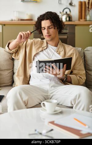 Ein junger Mann in stilvoller Kleidung skizziert Ideen nachdenklich zu Hause. Stockfoto