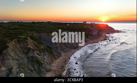 Aus der Vogelperspektive auf den Sonnenaufgang über den Mohegan Bluffs, das goldene Licht, das die zerklüfteten Klippen und die abstürzenden Wellen darunter malte, New Shoreham, Rhode Island, USA. Stockfoto