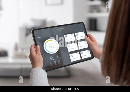 Person, die ein Tablet mit Smart-Home-Anwendung hält, um Klimaanlage, Waschmaschine und andere Haushaltsgeräte zu steuern Stockfoto