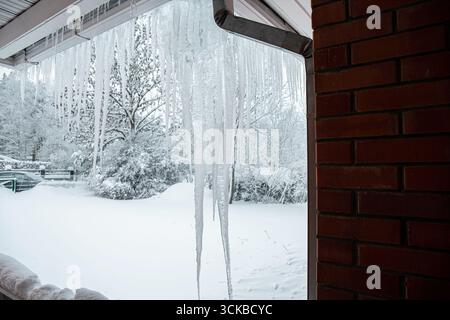 Große Eiszapfen hängen im Winter an der Regenrinne eines Privathauses. Gefahr des Bruchs und der Beschädigung der Regenrinnen. Stockfoto