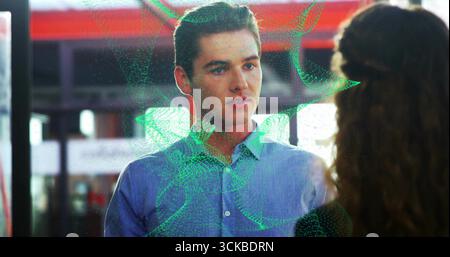 Stehender Mann in blauem Hemd, der Frau am Bahnhof zugewandt ist, mit einem wirbelnden grünen digitalen Hologramm. Technologie, Zusammenarbeit, Innovation, Futurismus, Bus Stockfoto
