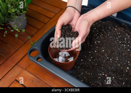Nahaufnahme der Hände, die einen kleinen Blumentopf mit Boden füllen, um ihn in einem Garten zu Pflanzen, Gartenarbeit, die Vorbereitung, Nachhaltigkeit und ec zeigt Stockfoto
