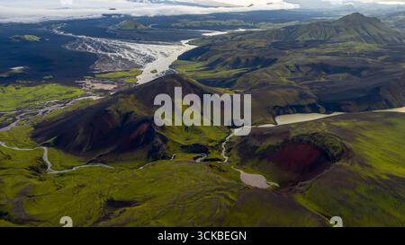 Aus der Vogelperspektive eines grünen Vulkankegels in Island, umgeben von dunklem Gelände, Flüssen, Seen, einem Gletscher und weitläufigen Ebenen im Hintergrund. Stockfoto