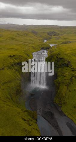 Dramatischer Blick aus der Luft auf den Skogafoss Wasserfall in Island, mit Wasser, das in einen nebeligen Pool stürzt, einem sich windenden Fluss und üppigen moosbedeckten Klippen. Stockfoto