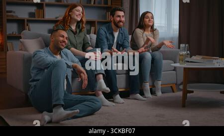 Vier multirassische Freunde schauen Fernsehen Lachen Lächeln sorglos zu Hause Party diskutieren Comedy lustige Kinofilme multiethnische Menschen Stockfoto