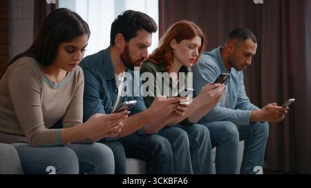 Millennial diverse vier Freunde überbeanspruchen Mobiltelefone süchtige Gadgets zu Hause Party multirassische Menschen Männer Frauen sitzen in der Schlange auf der Couch mit Stockfoto