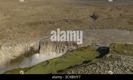 Der Dettifoss Wasserfall fällt in einen nebeligen Canyon, umgeben von felsigem Gelände und grünem Moos, aus der Vogelperspektive in Island. Stockfoto