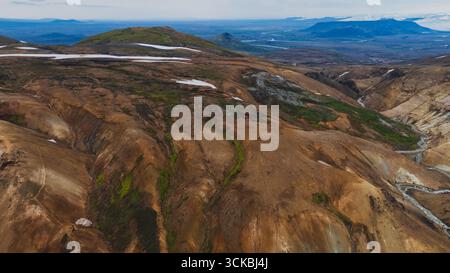 Aus der Vogelperspektive der isländischen Landmannalaugar-Region mit mehrfarbigen Rhyolithbergen, grünem Moos, Schneestücken, tiefen Tälern und weit entfernten Ebenen. Stockfoto