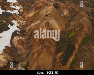 Dramatische Aussicht auf die mehrfarbigen Rhyolith-Berge in Landmannalaugar, Island, mit Schneelichtern, zerklüfteten Hängen und einem gewundenen Wanderweg. Stockfoto