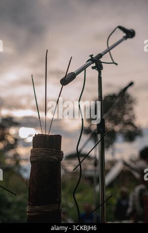 Nahaufnahme eines Mikrofonständers mit Räucherstäbchen auf einem Holzsockel vor einem bewölkten Himmel bei Sonnenuntergang Stockfoto