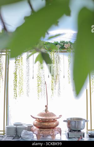Eine wunderschön gestaltete Catering-Einrichtung mit einem Kupfertopf und einem Edelstahltopf, umgeben von Grün und Blumendekoration, schaffen eine elegante Atmosphäre Stockfoto