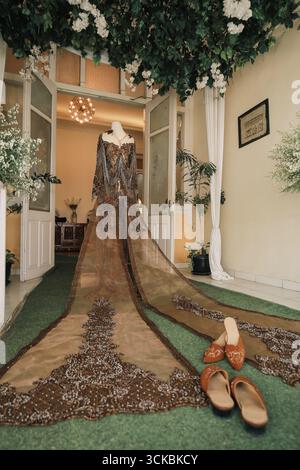 Ein atemberaubendes Brautkleid auf einer Schaufensterpuppe, mit komplizierten Perlen und einem langen Zug, in einem wunderschön dekorierten Raum mit Grün und Stockfoto