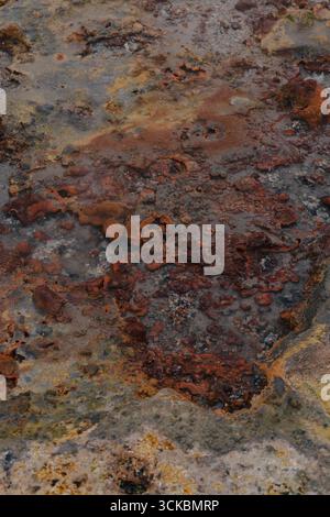 Nahaufnahme einer geothermischen Oberfläche in Island mit rostfarbenen Mineralablagerungen, gelben und grauen Flecken und ungleichmäßigen Texturen aus Geothermie Stockfoto