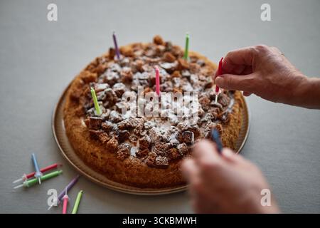 Senior-Mann, der Geburtstagskerzen auf hausgemachten Kuchen platziert Stockfoto