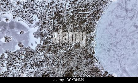 Luftbild eines schneebedeckten Geländes mit einem gefrorenen See auf der rechten Seite, strukturiertem Boden auf der linken Seite und einem kurvenreichen Pfad, der durch die Mitte führt. Stockfoto