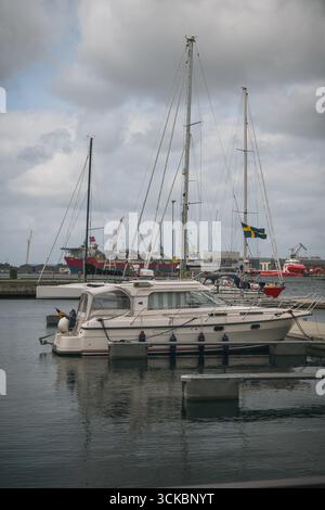Ein Yachthafen in Stavanger, Norwegen, mit angedockten Booten und Yachten, einer schwedischen Flagge auf einem Segelboot, Industriekränen und ruhigem Wasser unter bewölktem Himmel. Stockfoto