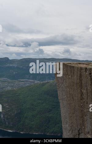Die berühmte Preikestolen Klippe erhebt sich über dem Lysefjord in Norwegen mit steilen Felswänden, üppigen grünen Hügeln, zerklüfteten Bergen und einem bewölkten Himmel. Stockfoto