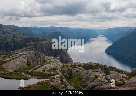 Blick auf Lysefjord in Norwegen, mit ruhigem Wasser, steilen felsigen Klippen, moosigen Stellen und einem bewölkten Himmel, der eine ruhige Atmosphäre schafft. Stockfoto