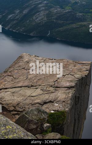 Die Preikestolen-Klippe ragt über den Lysefjord in Norwegen, mit einer flachen Felsoberfläche, steilen Abstürzen, ruhigen Fjordgewässern und einem entfernten Wasserfall. Stockfoto