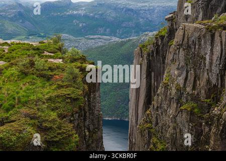 Blick auf die Preikestolen Klippen in Norwegen, mit einer engen Schlucht, üppigem Grün, zerklüfteten Felsen und Lysefjord umgeben von Hügeln und Bergen. Stockfoto