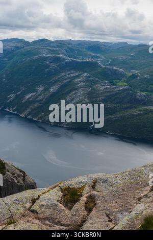 Lysefjord in Norwegen mit felsigem Gelände, steilen bewaldeten Bergen, einem kleinen Wasserfall und ruhigem Wasser unter einem bewölkten Himmel von einem erhöhten Aussichtspunkt. Stockfoto