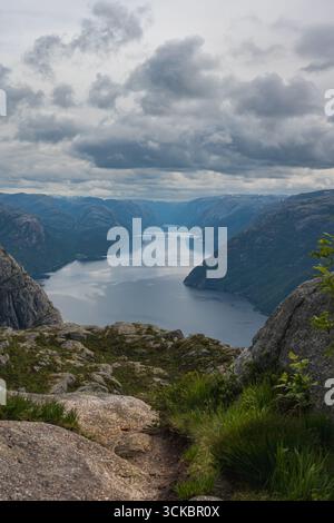 Der Lysefjord erstreckt sich bis in die Ferne, umrahmt von felsigen Klippen, üppigem Grün und steilen Bergen unter dicken, stimmungsvollen Wolken in Norwegen. Stockfoto