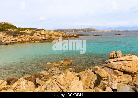 Goldene Felsen und kristallklares türkisfarbenes Wasser auf Cala Corsara, Spargi Island, mit zerklüfteter Küste und ruhiger mediterraner Landschaft. Stockfoto