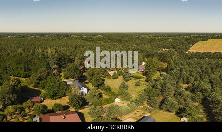 Panoramablick auf eine ländliche Gegend mit roten und grauen Häusern, dichtem Wald, offenen Grünflächen, Ackerland und einem klaren blauen Himmel. Stockfoto