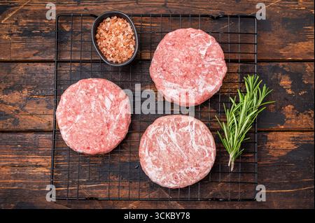 Gefrorene Fleischpasteten, bereit zum Grillen, Forcemeat von Schwein und Rindfleisch für Burger. Hölzerner Hintergrund. Draufsicht Stockfoto