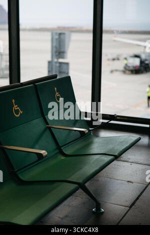 Ausgewiesene Flughafensitze für behinderte Passagiere mit Blick auf den Asphalt Stockfoto