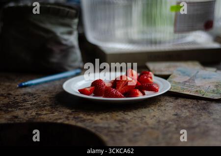 Teller mit frisch geschnittenen Erdbeeren auf rustikalem Küchentisch mit zwanglosem Hintergrund, gemütlichem Alltagsstillleben. Stockfoto