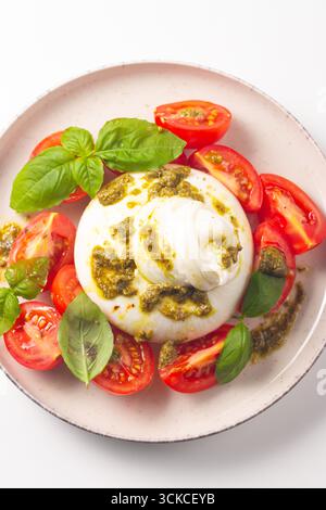 Burrata-Käse-Caprese-Salat mit Kirschtomaten, Olivenöl, Pesto und Gewürzen. Frischkost-Konzept. Stockfoto