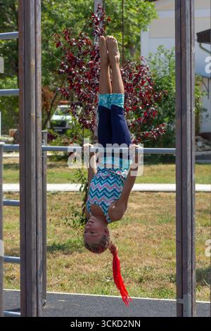 Ein Kind hängt kopfüber an einer Klimmstange und zeigt im Freien Wendigkeit und Mut Stockfoto
