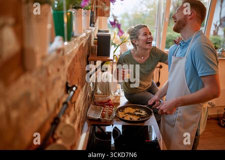 Netter junger Mann, der einen freudigen Moment in einer Küche teilt. Mann kocht Abendessen. Zweisamkeit, Spaß, Lifestyle-Konzept. Stockfoto