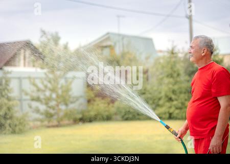 Mann, der Rasen bewässert. Bewässerungssystem Rasen-Sprinkler sprühen Wasser über frisches grünes Gras im Garten am Sommermorgen in heller Außensonne mit natürlichem verschwommenem Hintergrund. Nahaufnahme, Kopierbereich. Stockfoto