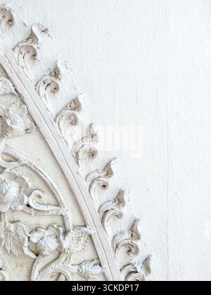 Eine Nahaufnahme eines weißen Stuckgemäldes an einer Tempelwand in Thailand, das traditionelle, komplizierte Blumen- und kunstvolle Muster mit natürlichem Licht und en zeigt Stockfoto